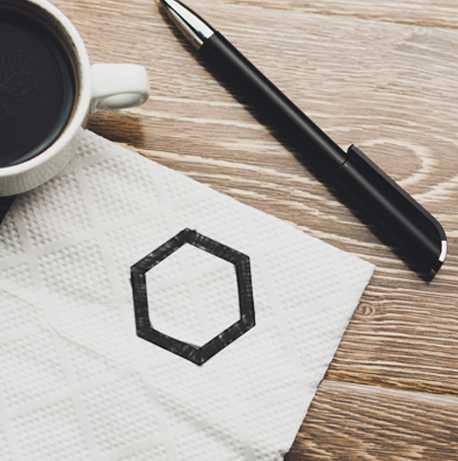 A pen, coffee cup, and napkin with a hexagon doodled on it